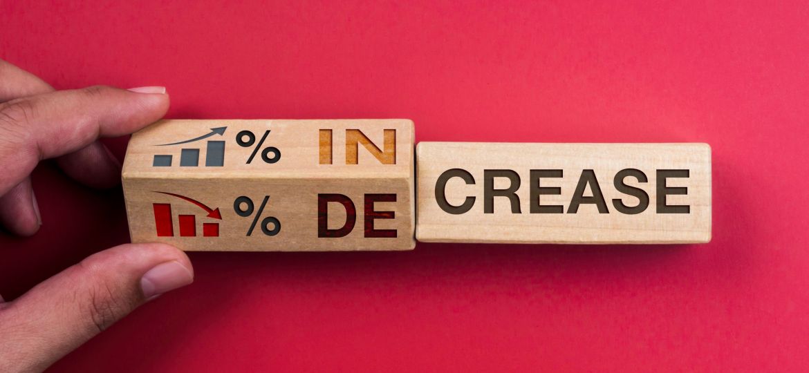 Decrease and increase percentage business concept. Words "INCREASE" on wooden block changing to "DECREASE," turning by hand with percentage symbol, growth and down chart graph icon on red background.